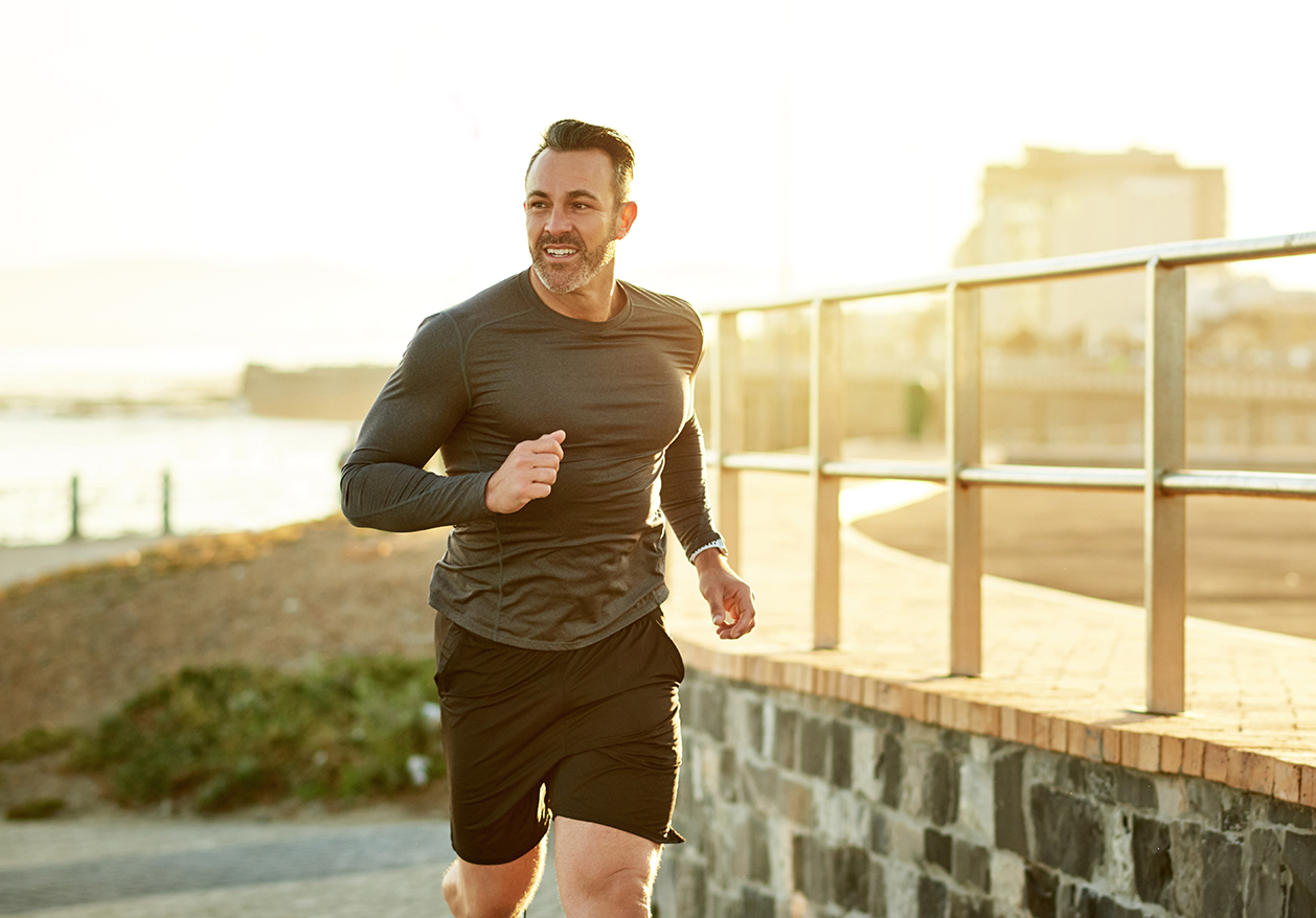 Smiling man jogging along the coast at sunset